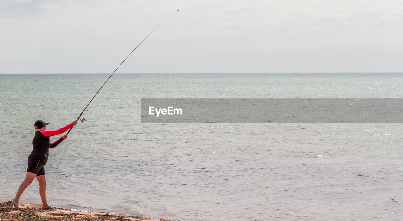 MAN FISHING AT SEA AGAINST SKY