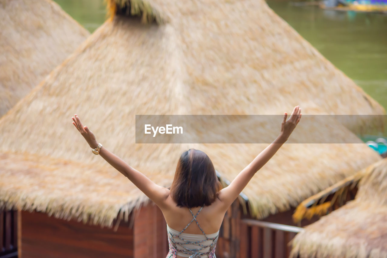 REAR VIEW OF WOMAN WITH ARMS RAISED IN PARK