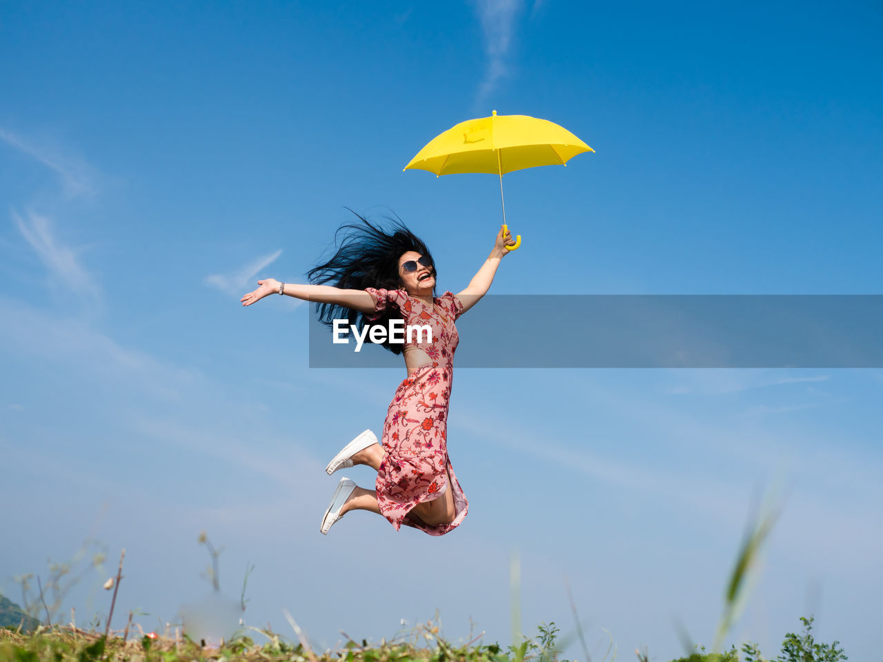 Woman jumping while holding umbrella against sky