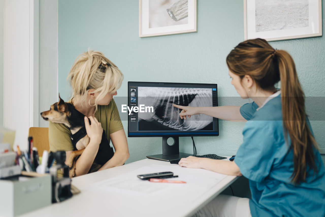 Female veterinarian showing x-ray on computer to woman with dog in doctor's office