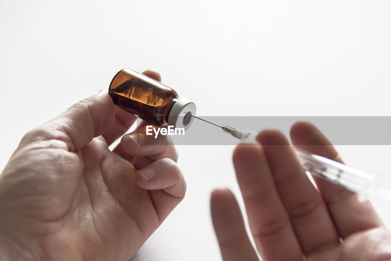 Cropped hands filling syringe with medicine against white background