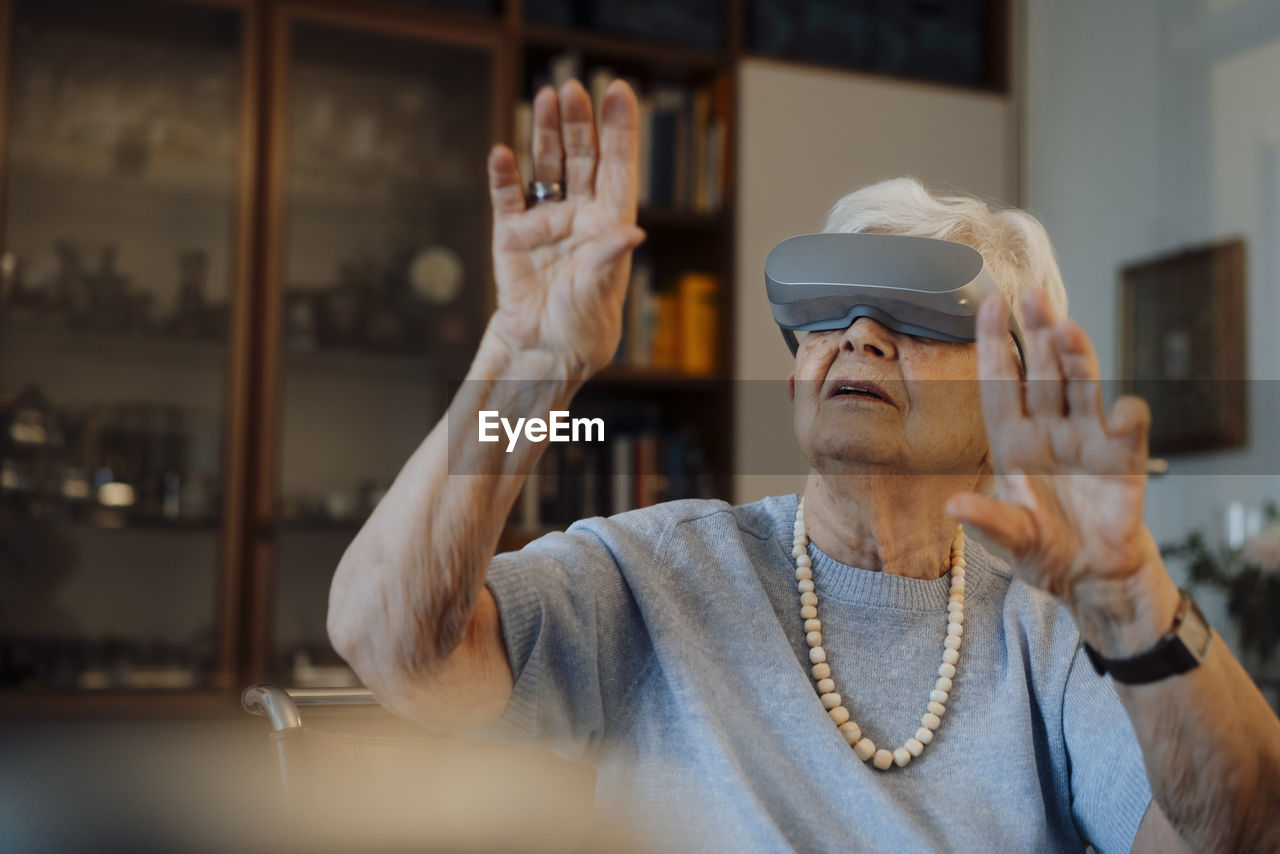 Senior woman wearing virtual reality simulator gesturing at home
