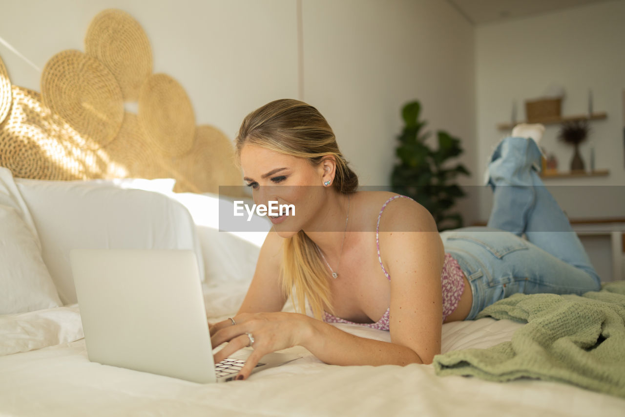 Woman works at home in her bedroom with laptop on her bed. woman lying down. home office.  notebook. 