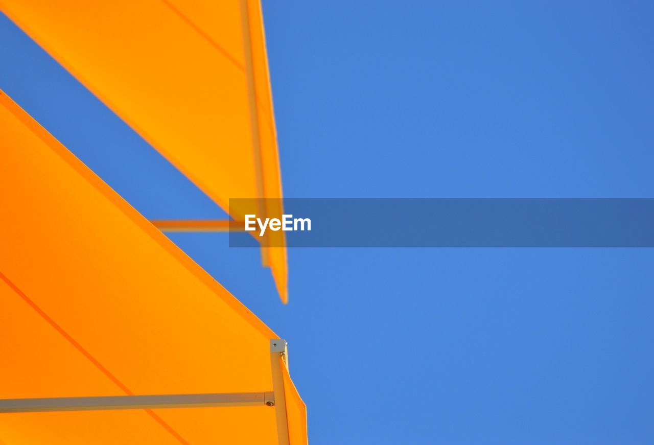 Low angle view of yellow umbrella against clear blue sky