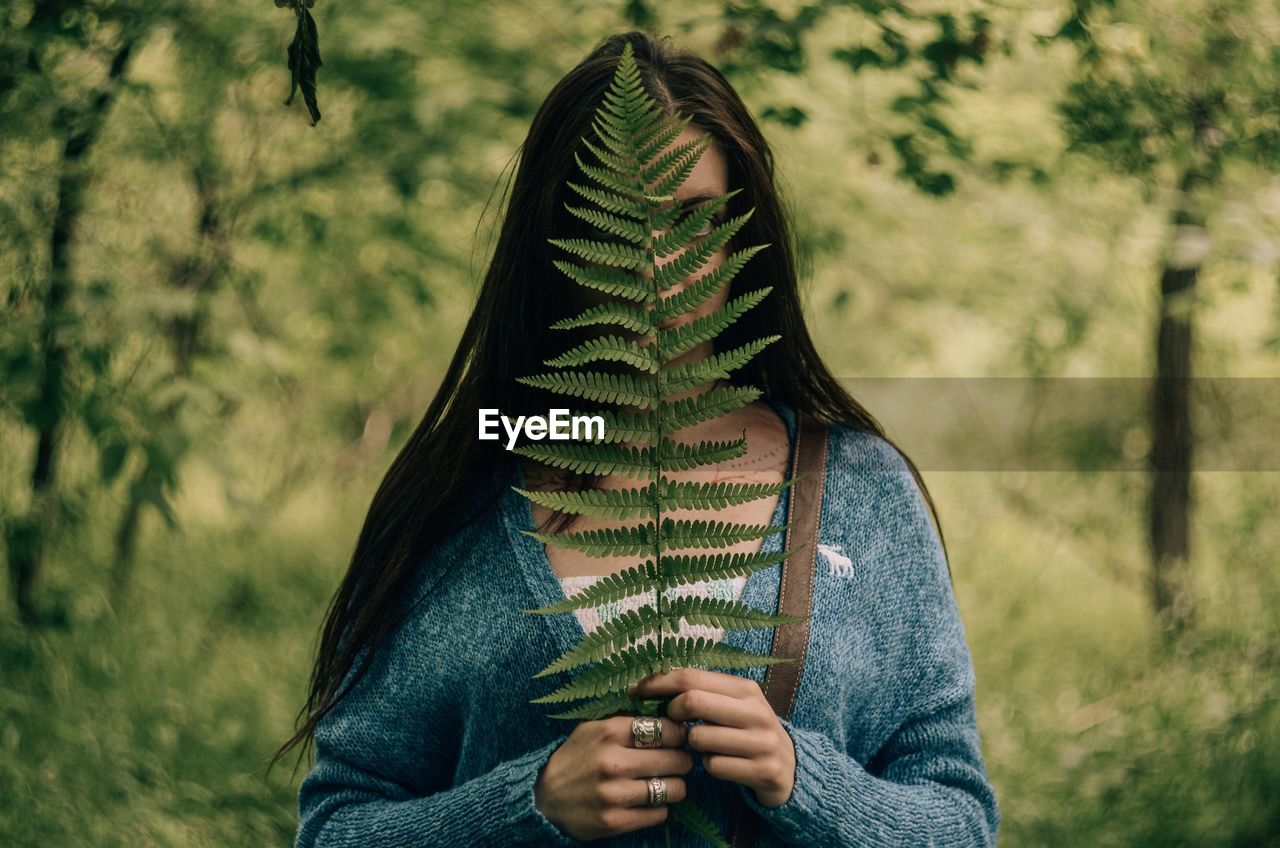 MIDSECTION OF WOMAN HOLDING PLANT IN FIELD