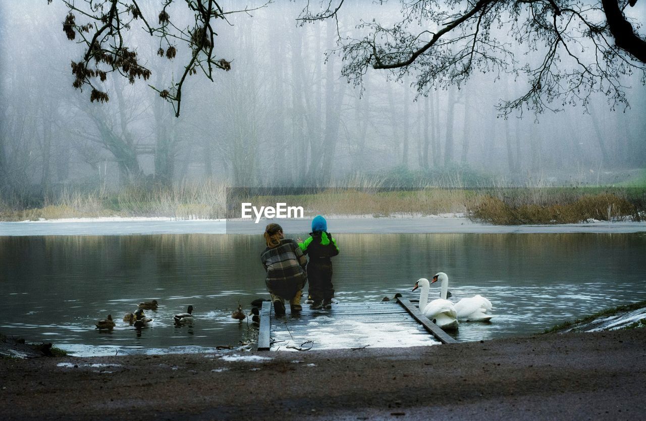 Rear view of mother with child at lakeshore during foggy weather