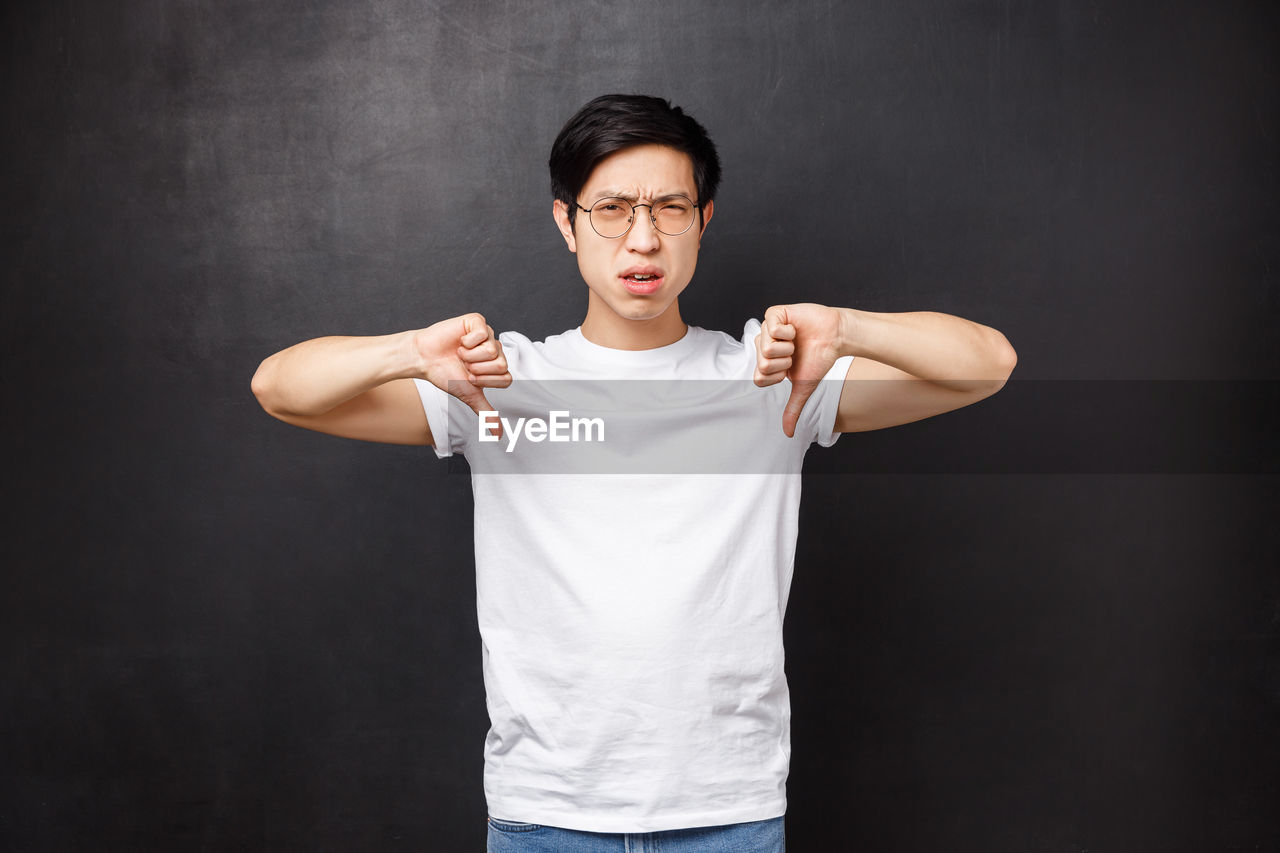 Man showing thumbs down gesture against black background