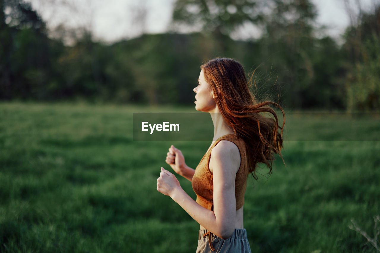 side view of young woman looking away while standing on field