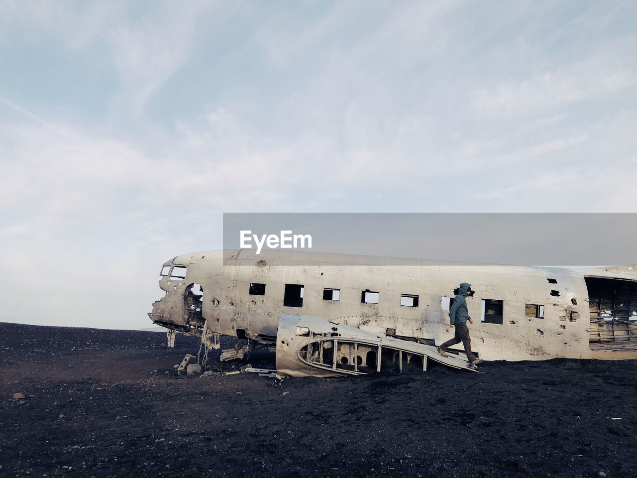 Side view of man walking by abandoned airplane against sky