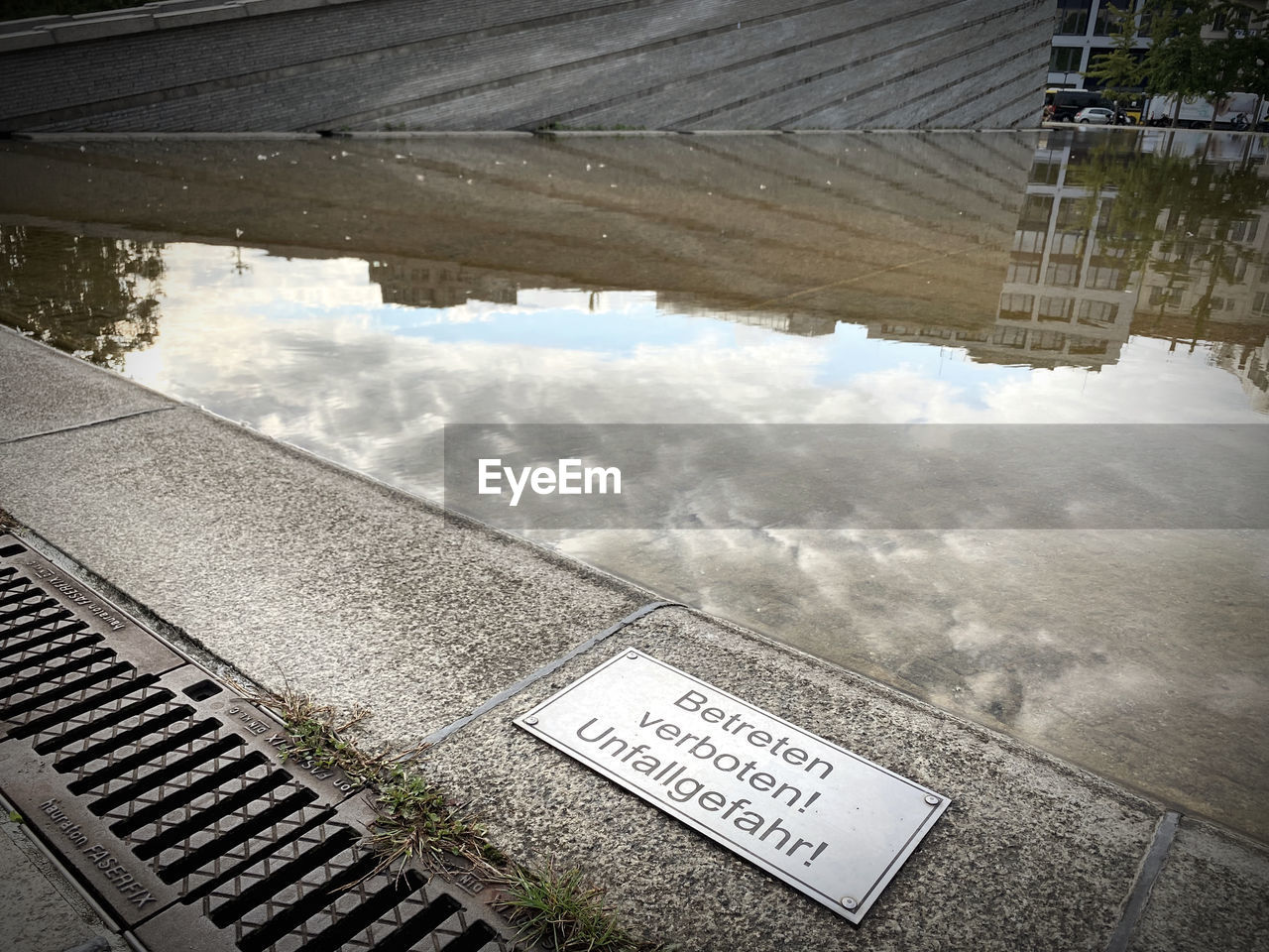 reflection, text, day, high angle view, communication, water, architecture, no people, sign, nature, snow, built structure, western script, urban area, outdoors, white, puddle, city, roof, transportation, wall