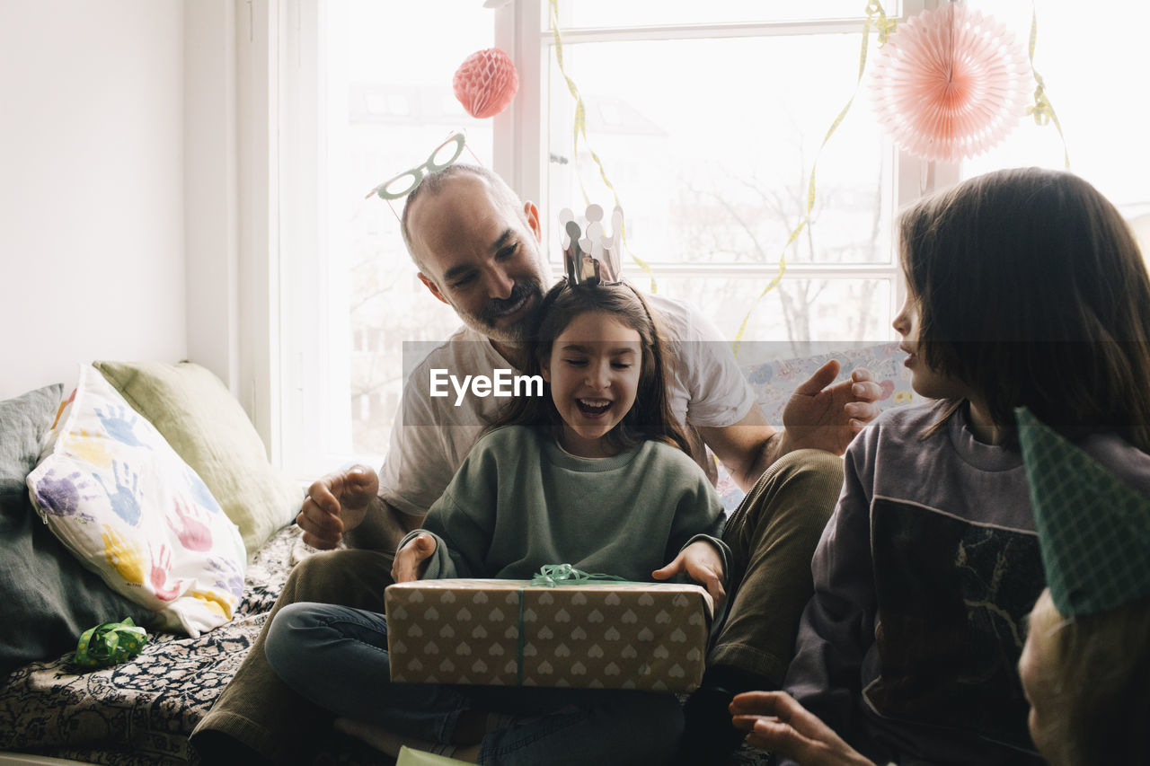 Surprised girl holding birthday present while sitting with brother and father at home