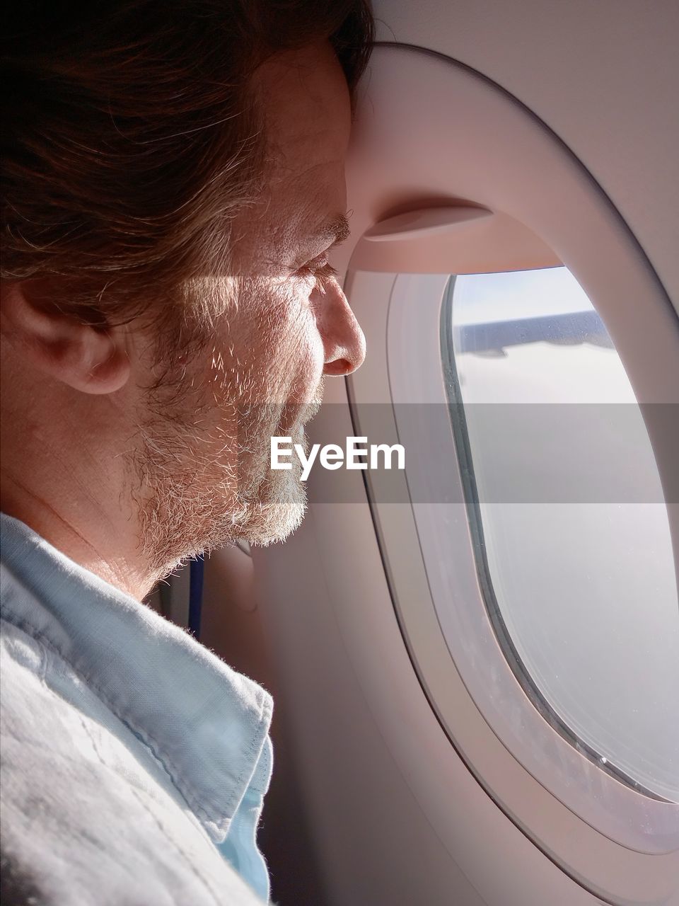 Side view of man looking out of window sitting in airplane 