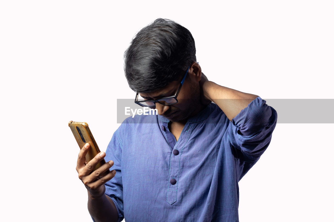 one person, white background, studio shot, person, adult, hand, cut out, wireless technology, indoors, technology, communication, holding, young adult, clothing, waist up, men, finger, looking, mobile phone, sleeve, glasses, black hair, looking down, portable information device, smartphone, copy space, casual clothing, business, arm, eyeglasses, human face, standing, portrait, telephone