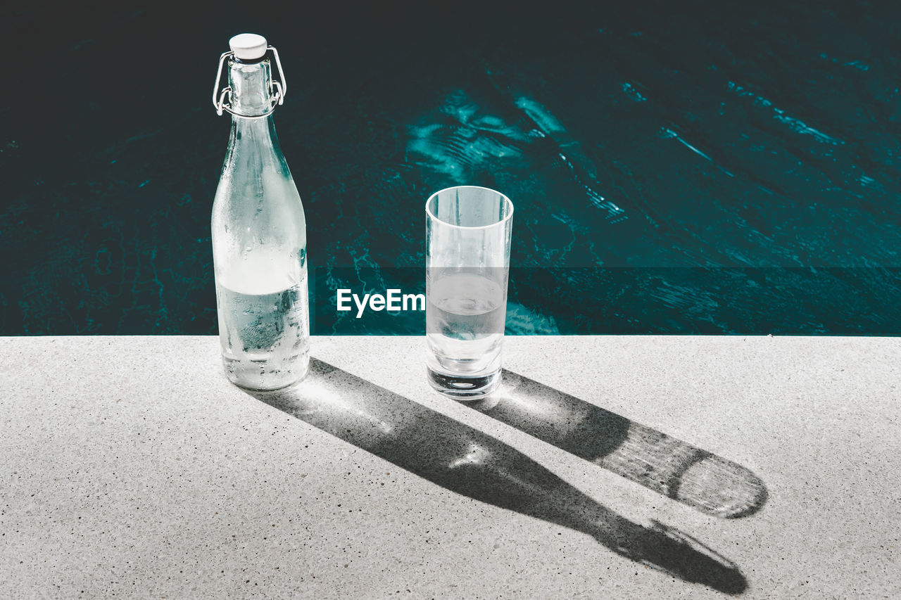 Close-up of bottle and glass on retaining wall by lake