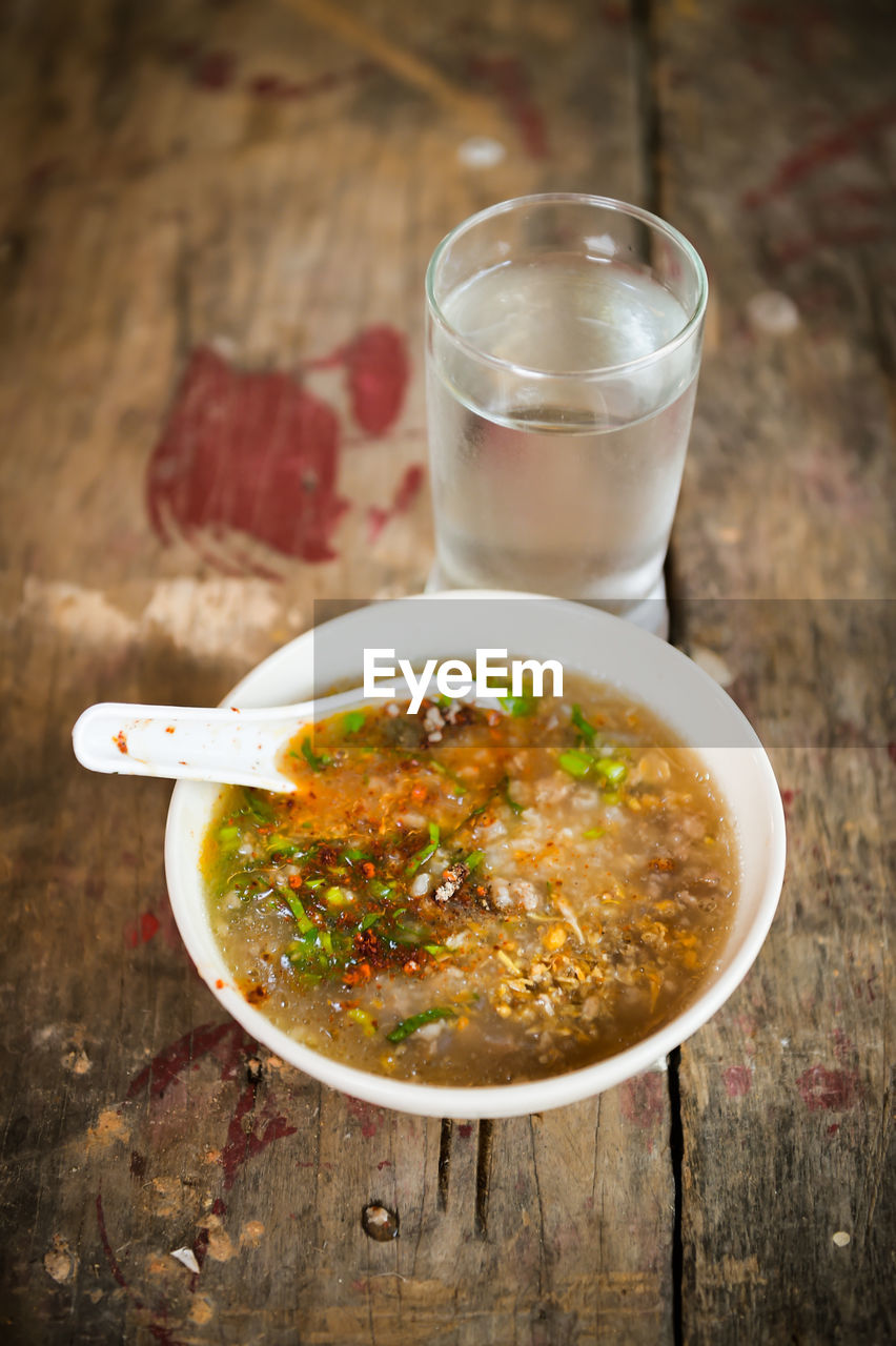 High angle view of soup in bowl and drinking glass on wooden table