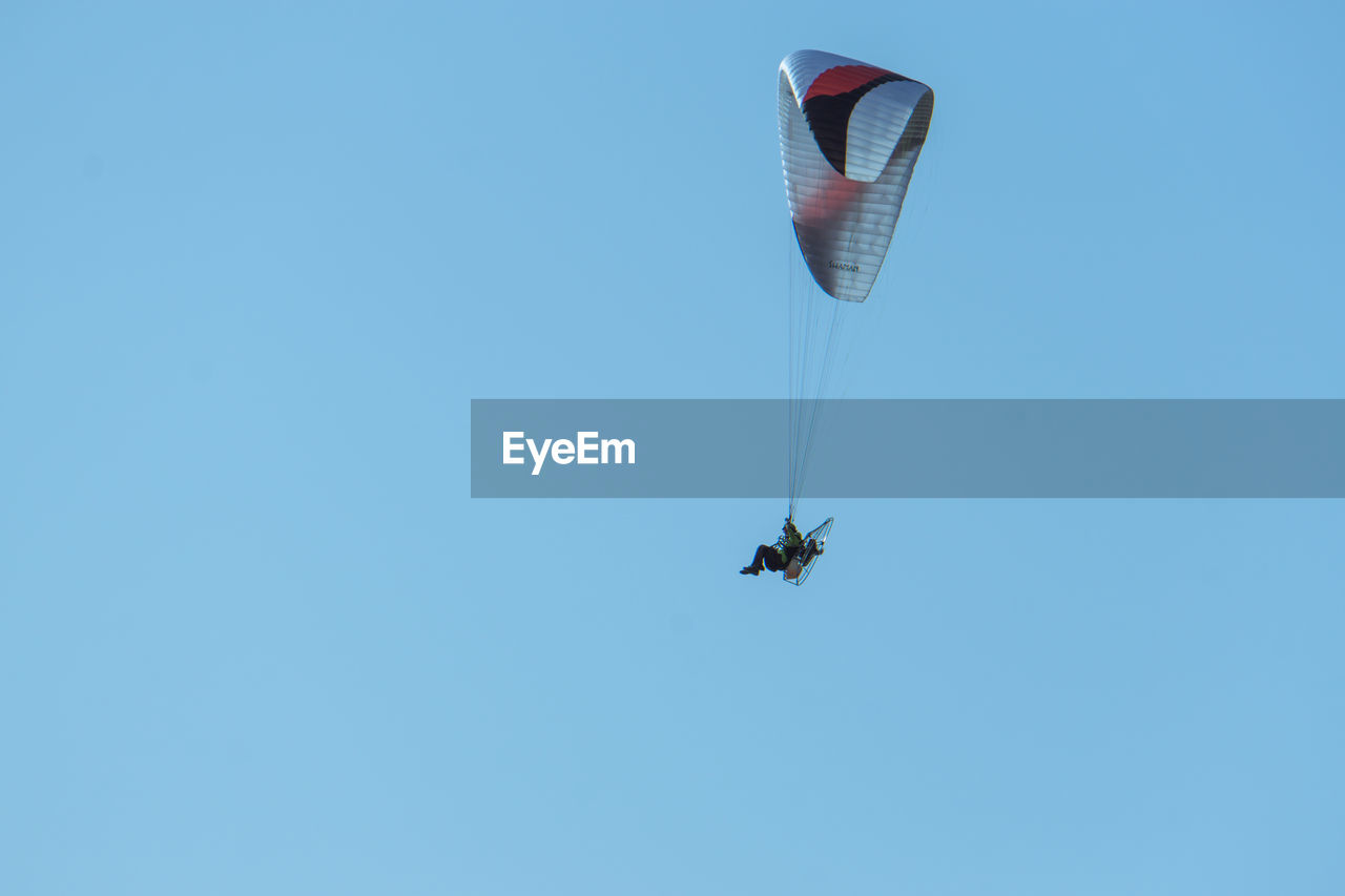 Low angle view of man powered paragliding in clear blue sky
