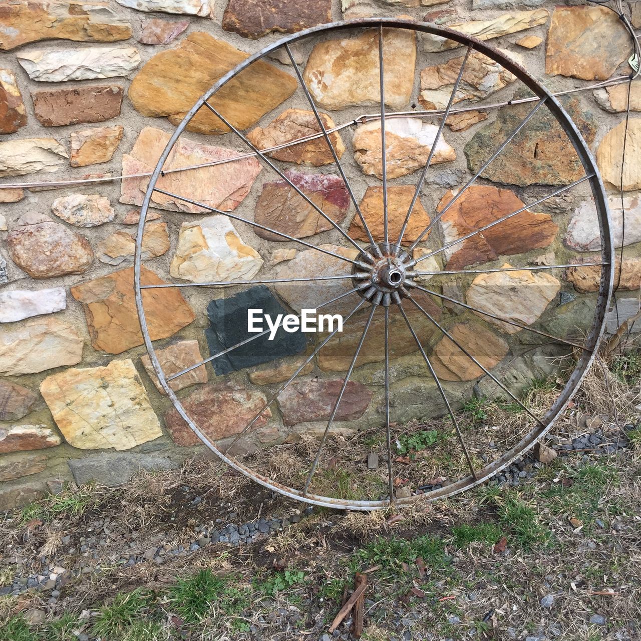 Close-up of old wheel against stone wall