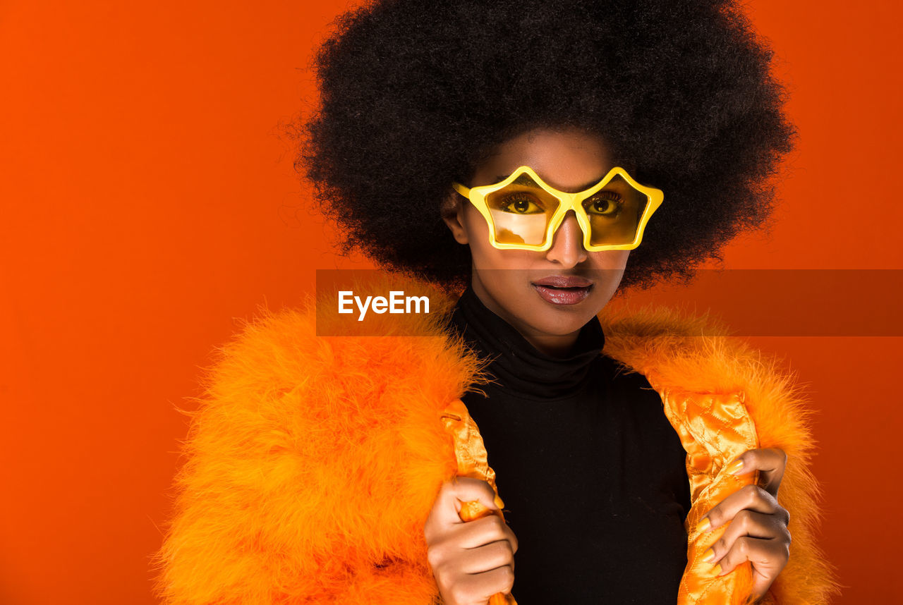 Portrait of beautiful young woman wearing sunglasses against orange background