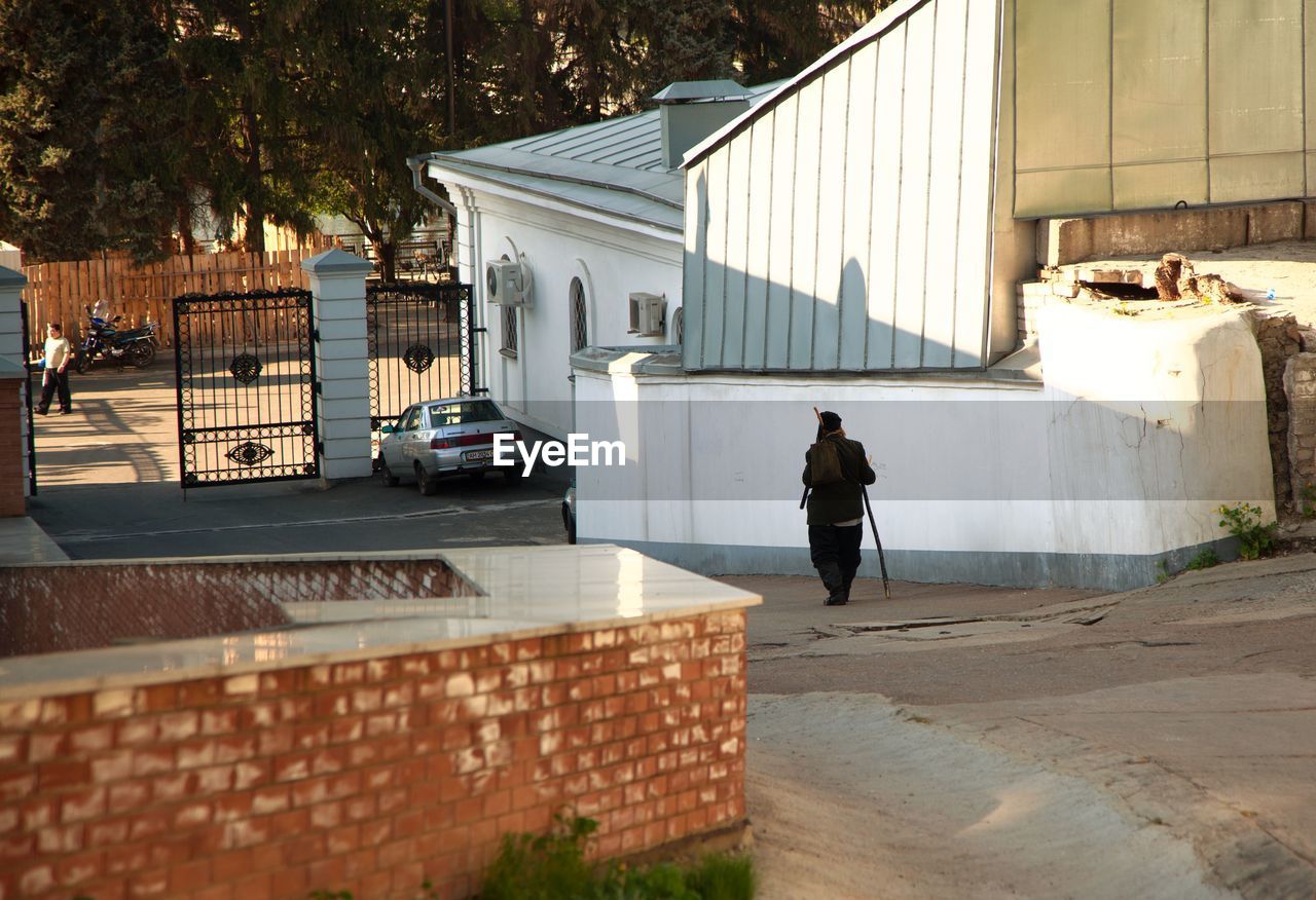 REAR VIEW OF MAN WALKING BY BUILDING