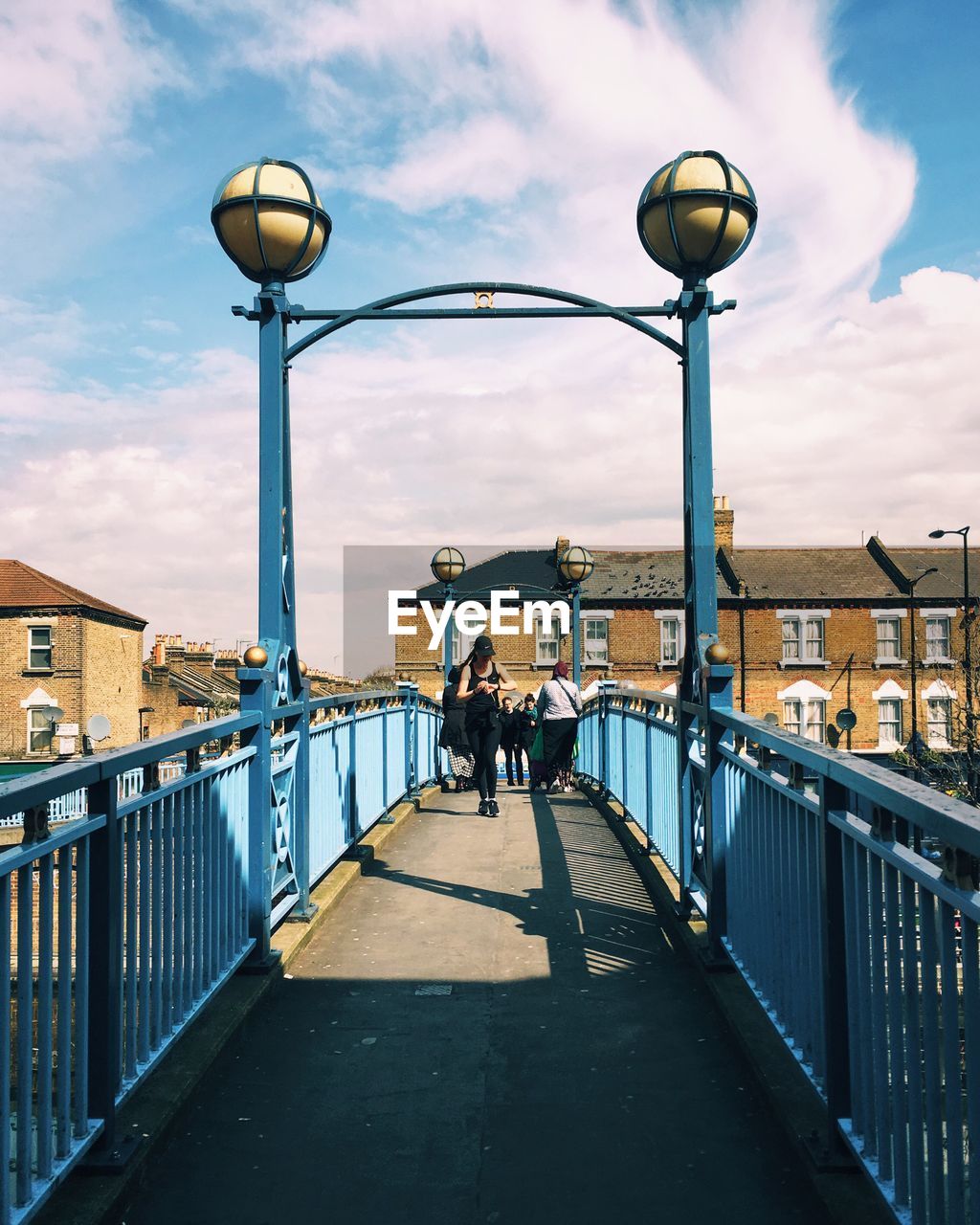 People walking on footbridge against sky in city