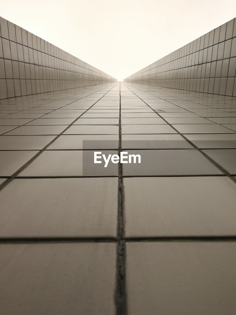 Empty tiled walkway against clear sky