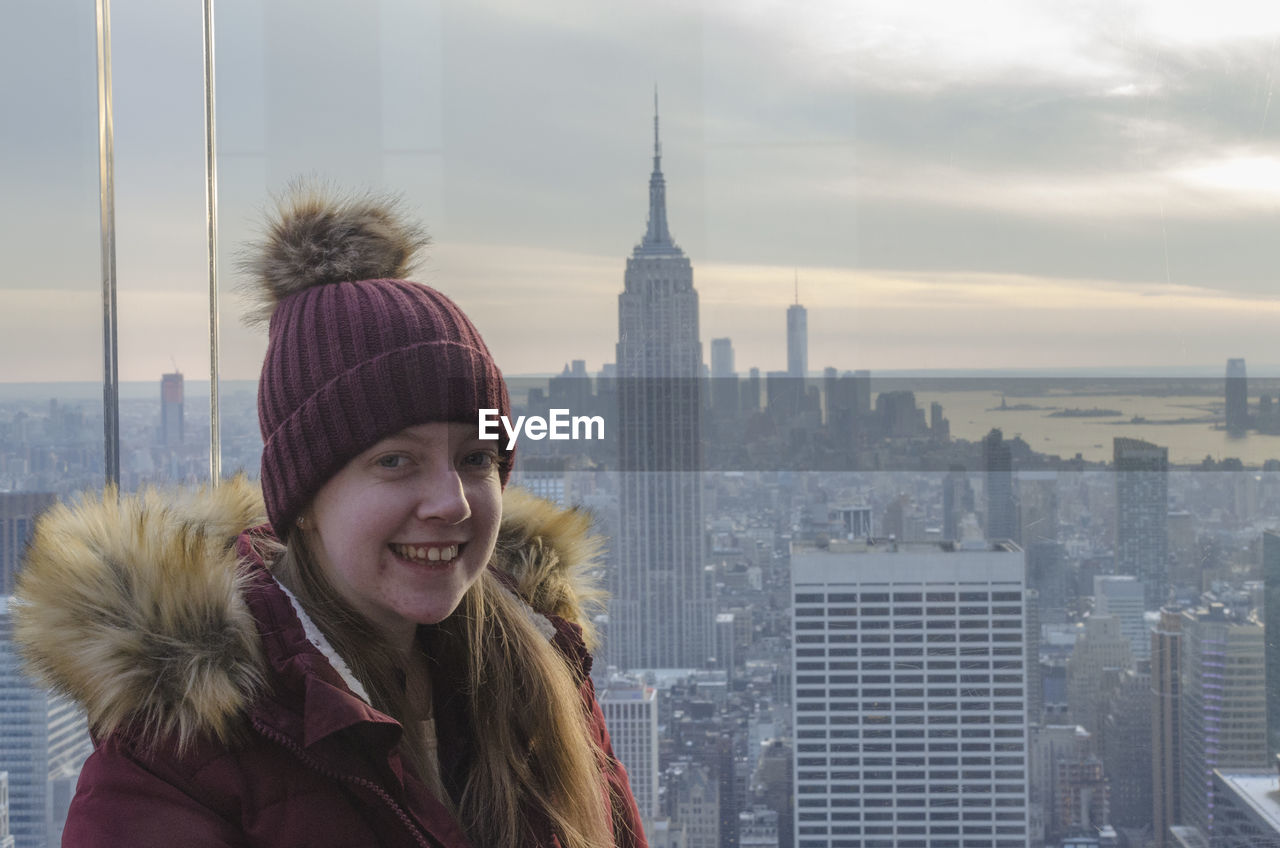 Portrait of smiling young woman standing by window in city