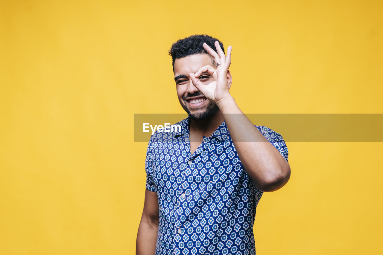 Happy man showing ok gesture while standing against yellow background