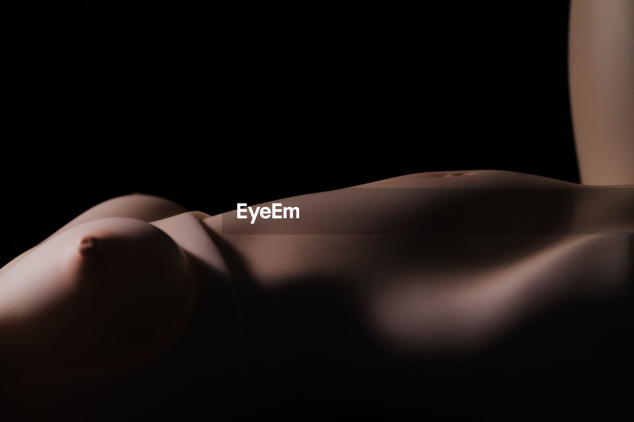 MIDSECTION OF WOMAN LYING DOWN ON BLACK BACKGROUND