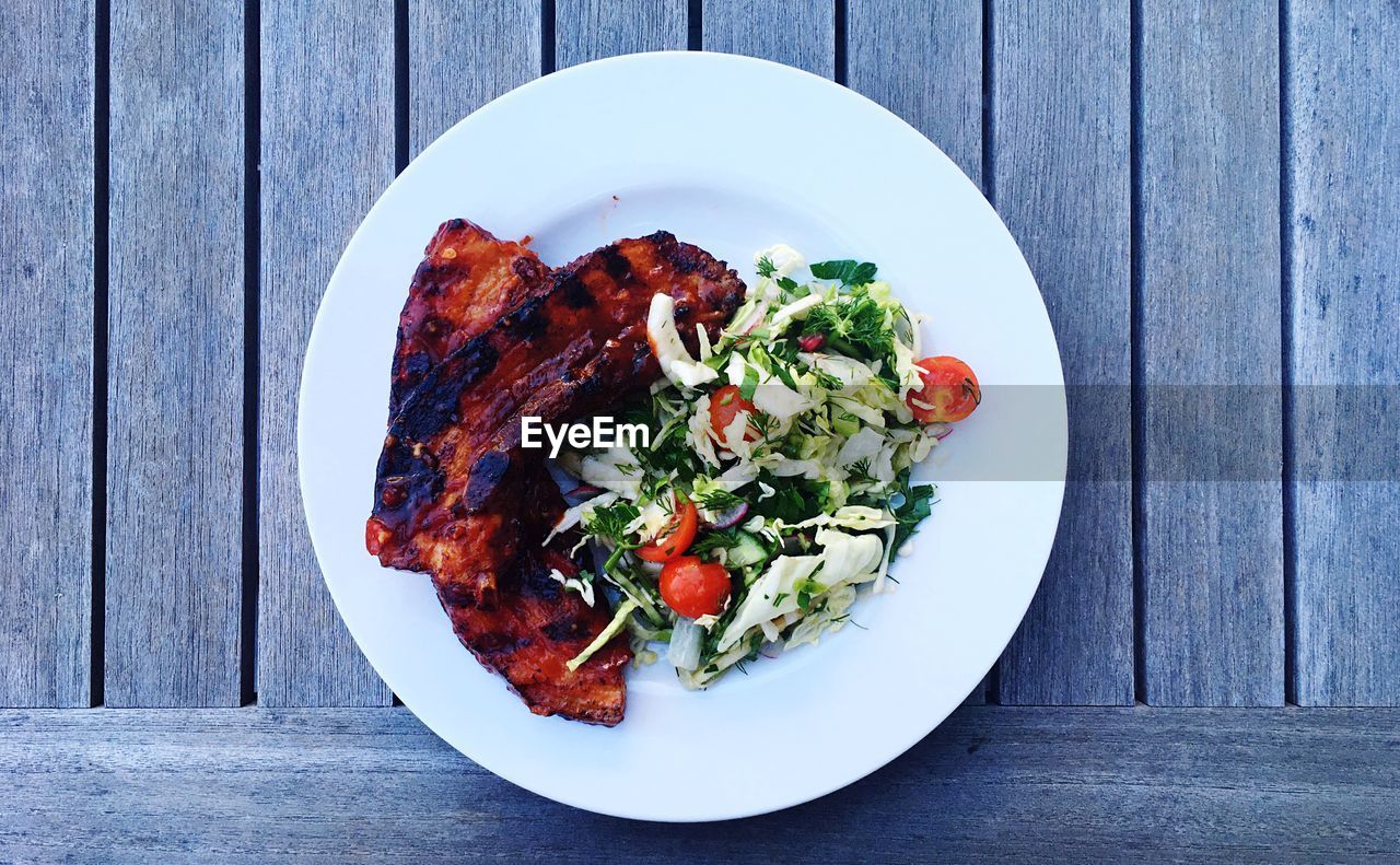 High angle view of salad and pork in plate on wooden table