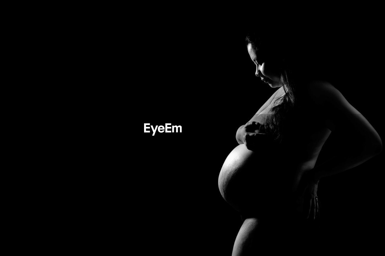 Pregnant woman standing against black background