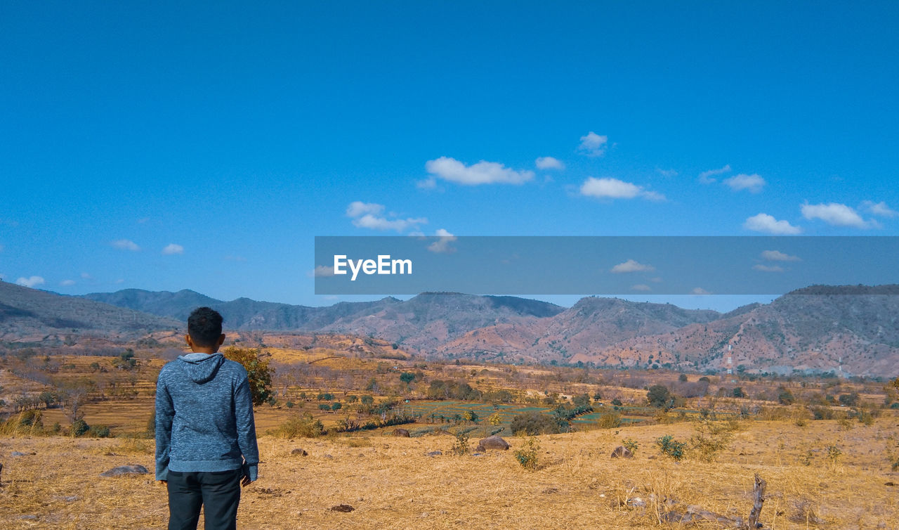 Rear view of man standing on landscape against sky