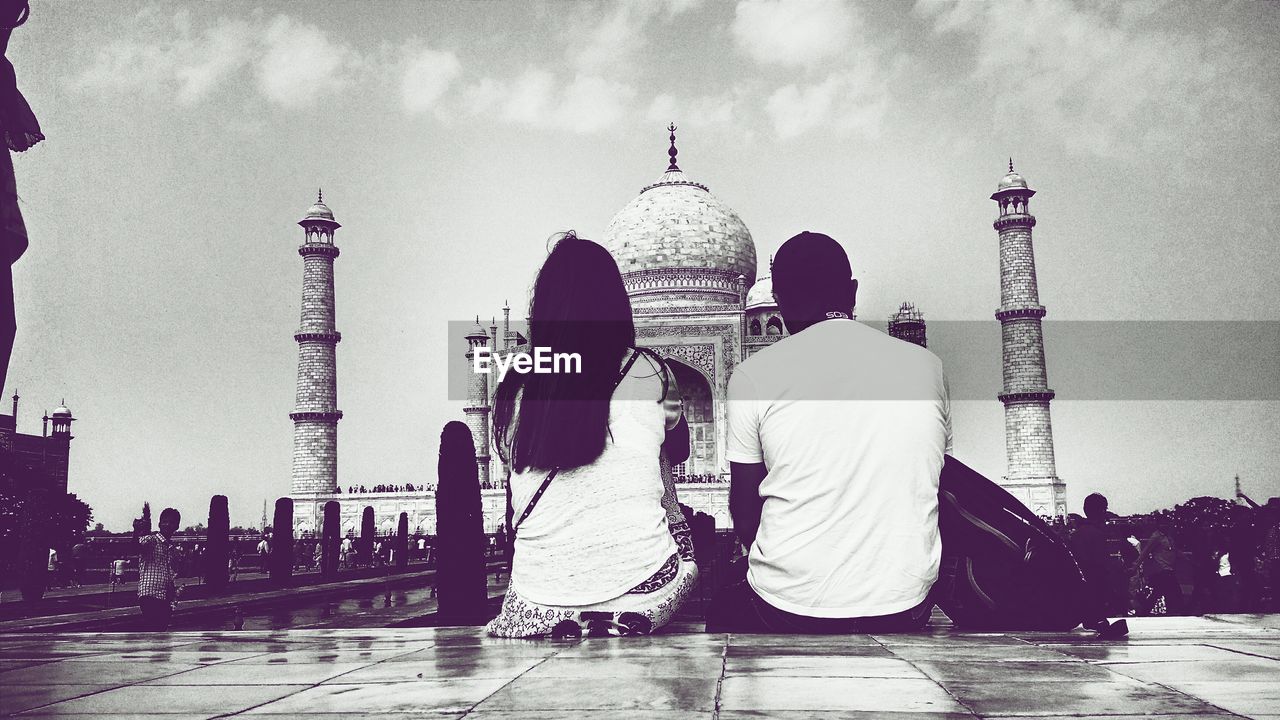 Rear view of man and woman sitting against taj mahal