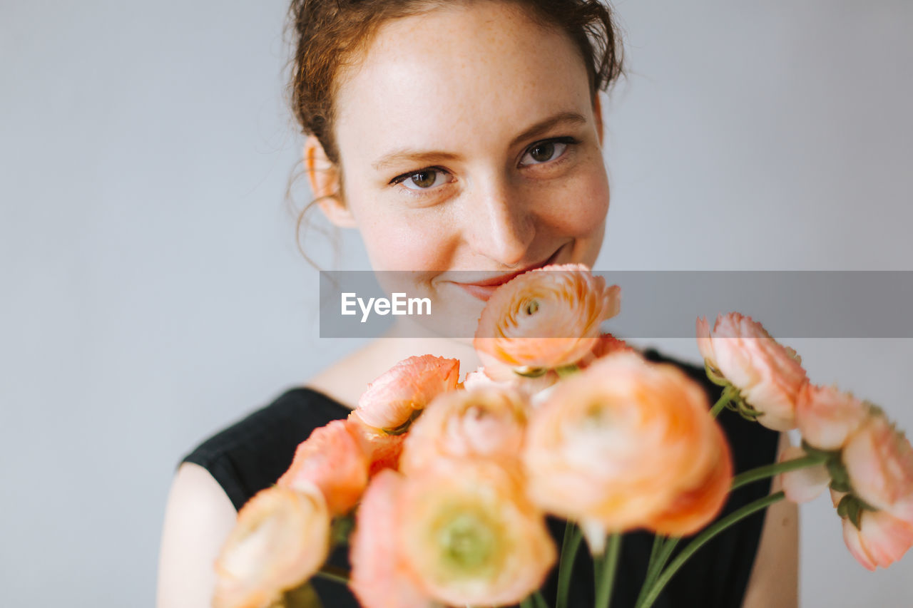 Portrait of smiling woman with flowers against wall