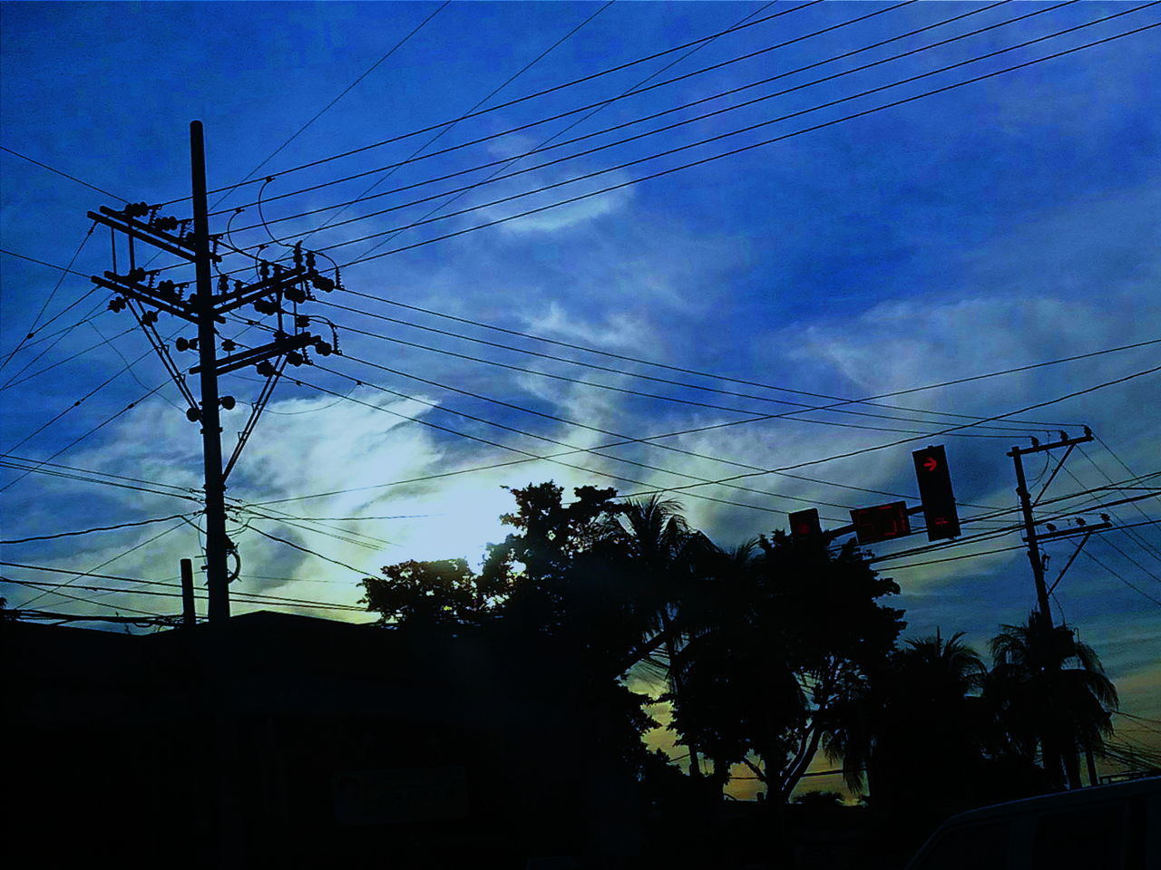 Low angle view of silhouette trees and electricity pylon against cloudy sky