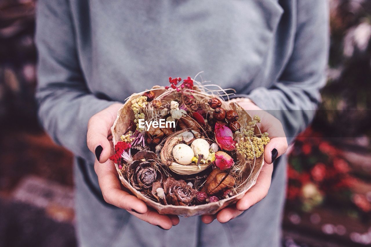 Midsection of woman holding petals and pine cone