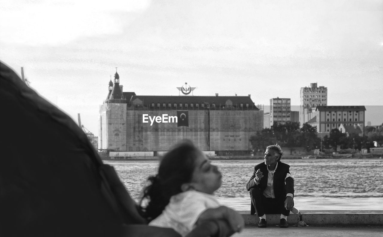 PEOPLE SITTING IN PARK AGAINST BUILDINGS IN CITY