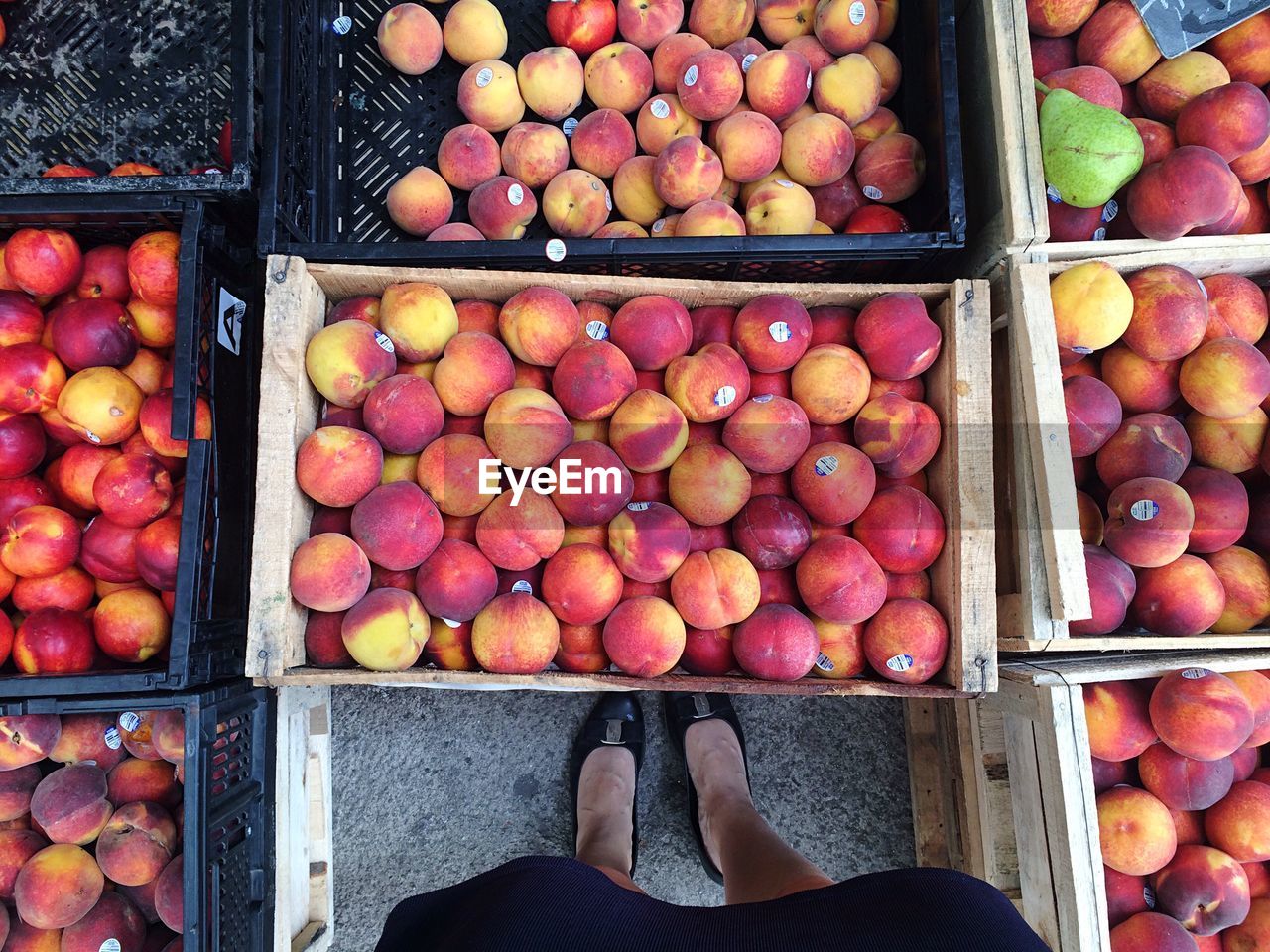 Directly above view of woman standing amidst organic peach crates in market