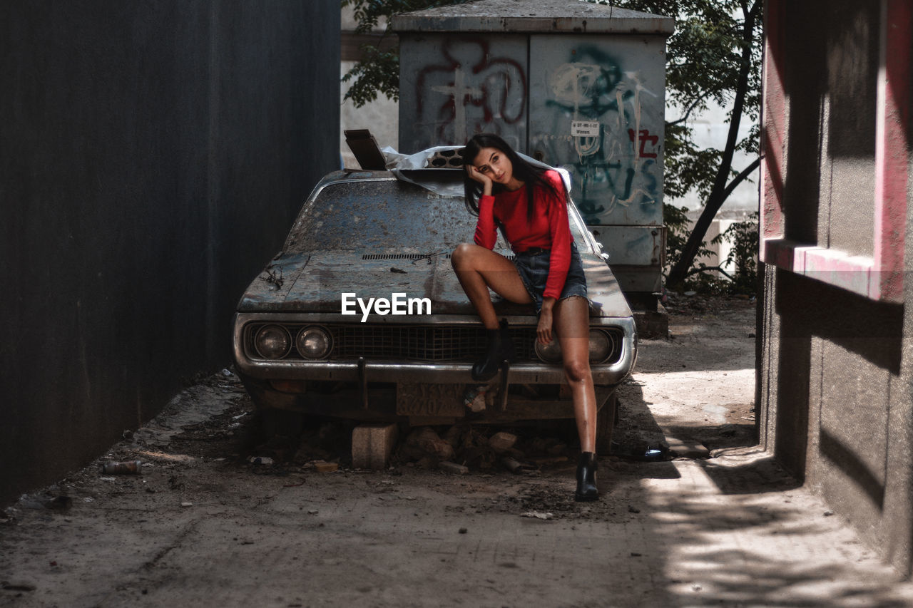 Full length of woman sitting on abandoned car