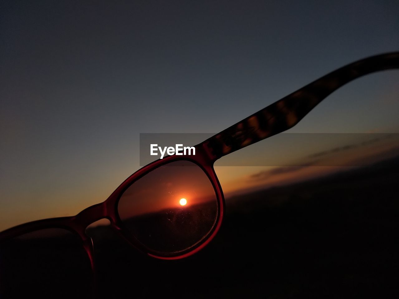 CLOSE-UP OF SUNGLASSES AGAINST ORANGE SKY