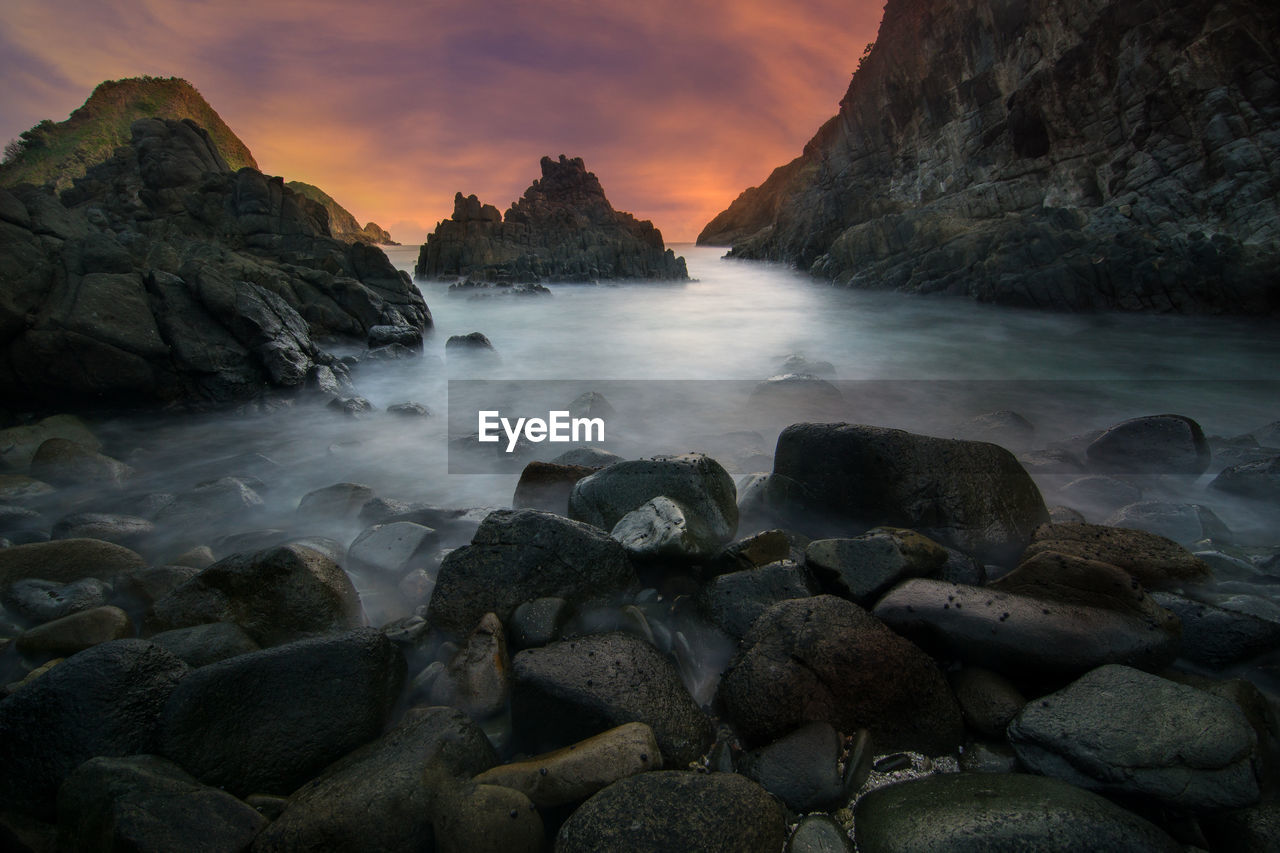 Rocks on sea shore against sky during sunset