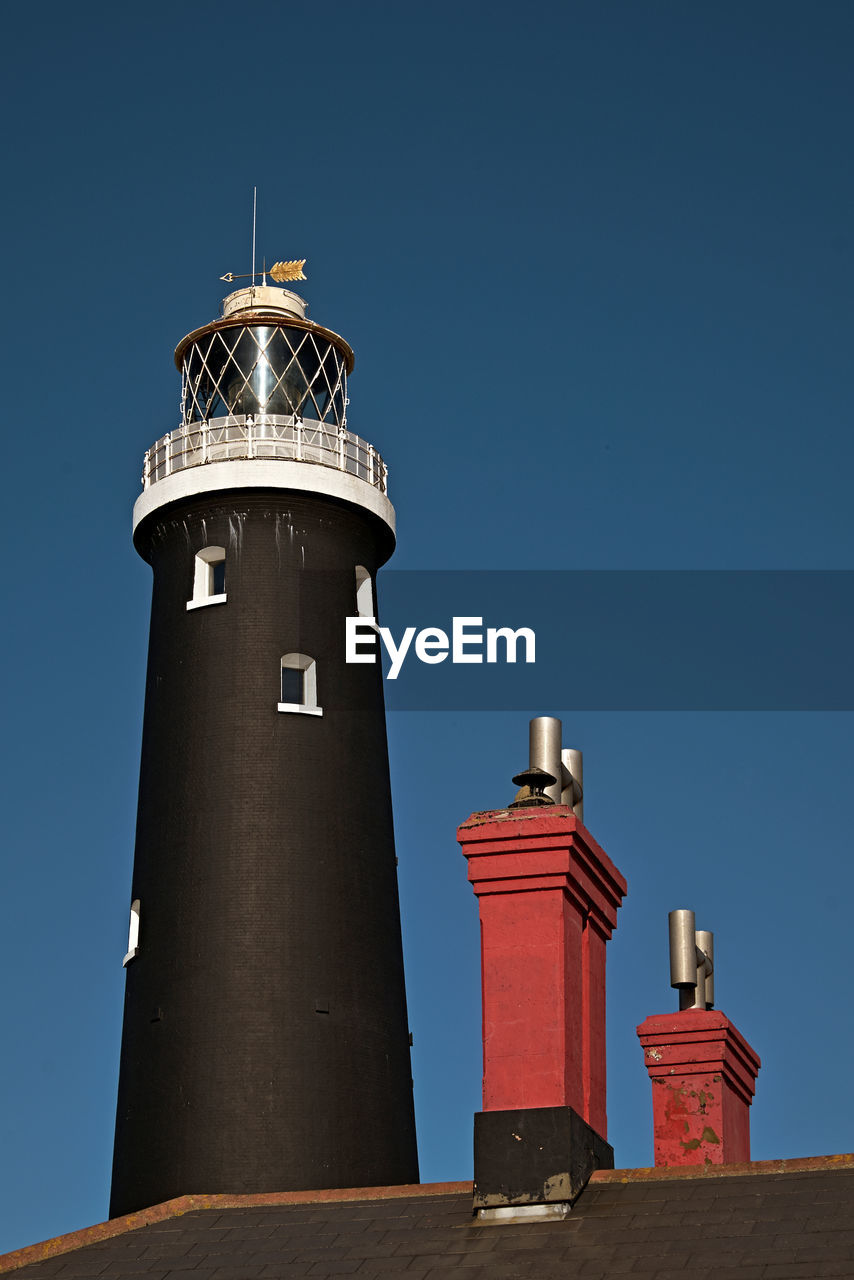 LOW ANGLE VIEW OF LIGHTHOUSE BY BUILDING AGAINST CLEAR BLUE SKY