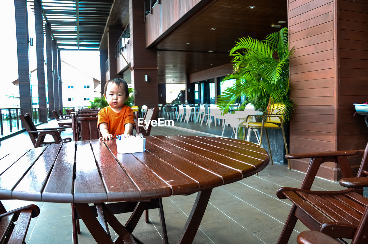 Boy standing on wooden chair at restaurant