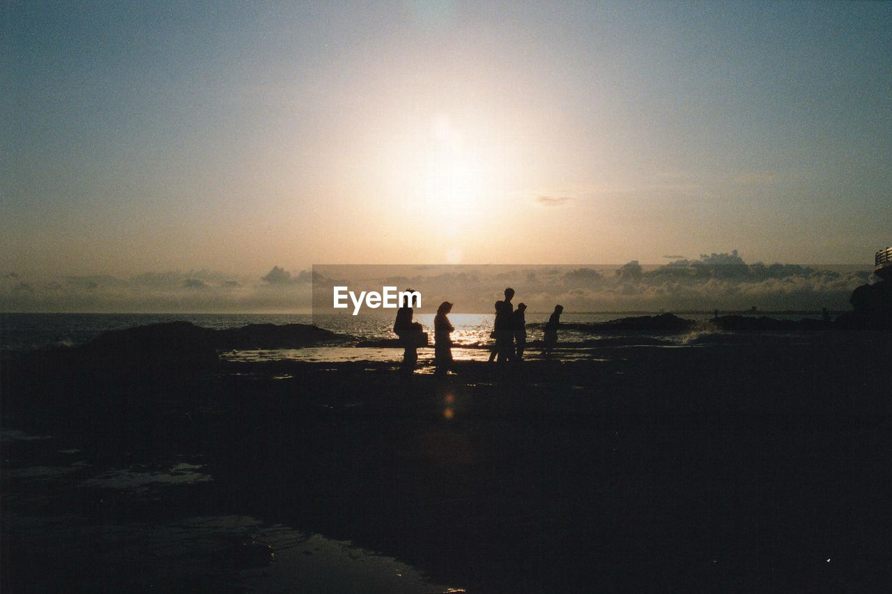 Silhouette people walking on calm beach