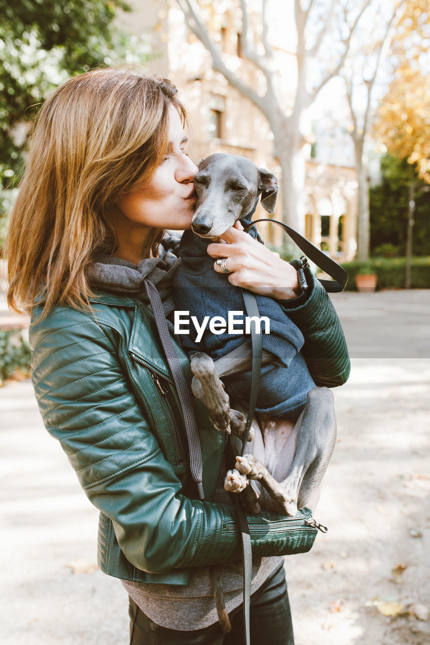 Cute young woman hugging and kissing her italian greyhound small breed of dog.  outdoor photo