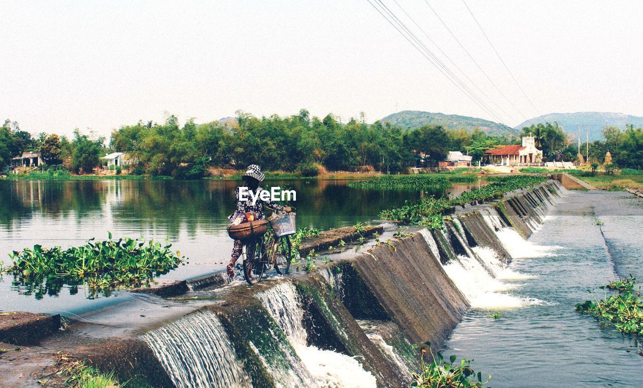 Rear view of woman with bicycle walking on dam