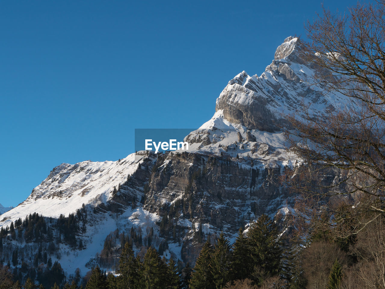 Low angle view of snowcapped mountains against clear blue sky