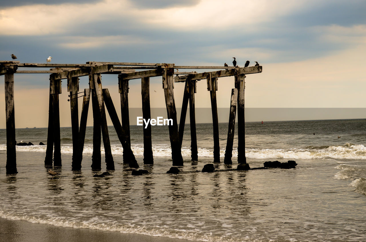 Abandoned wooden pier at beach against sky