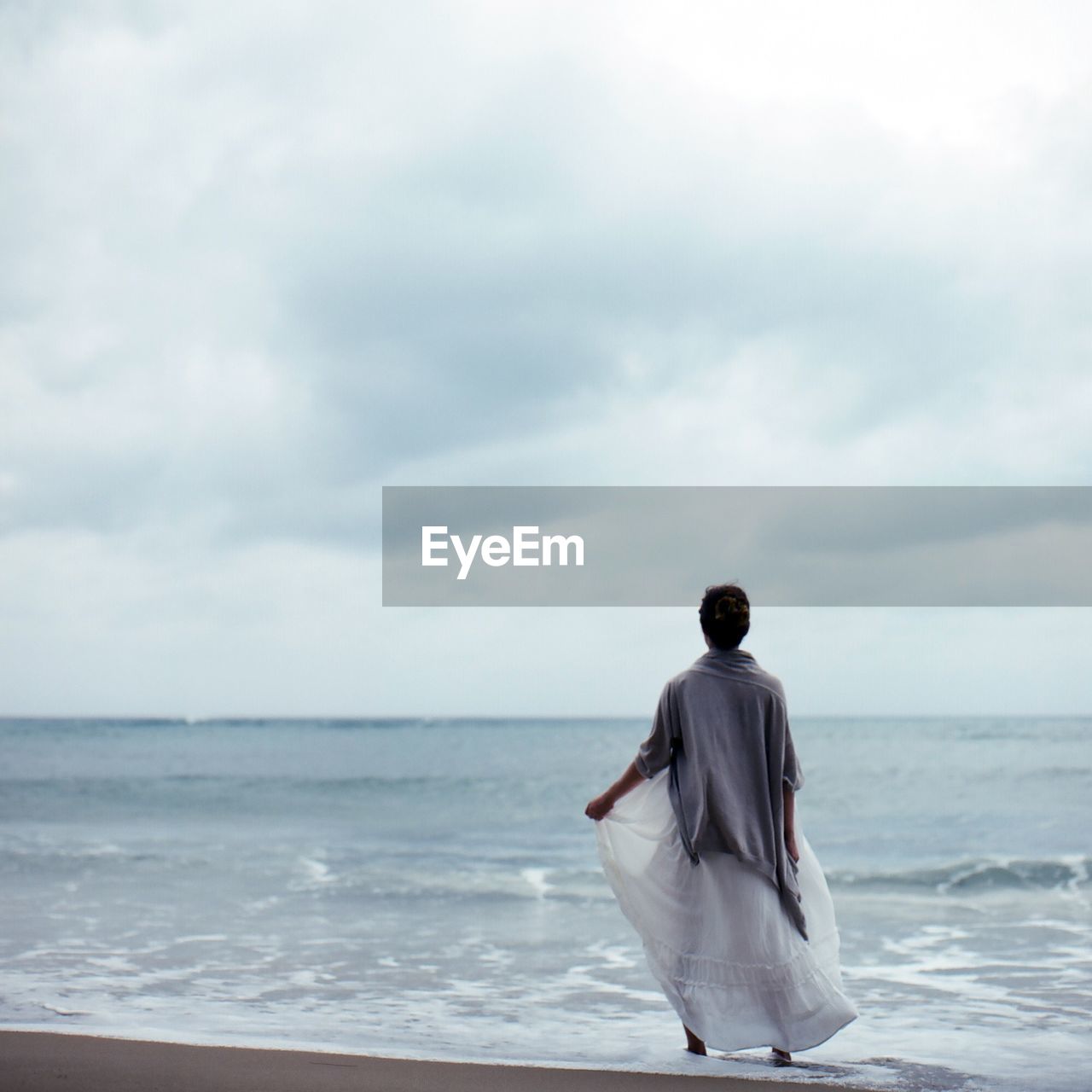 Rear view of woman standing at sea shore against sky