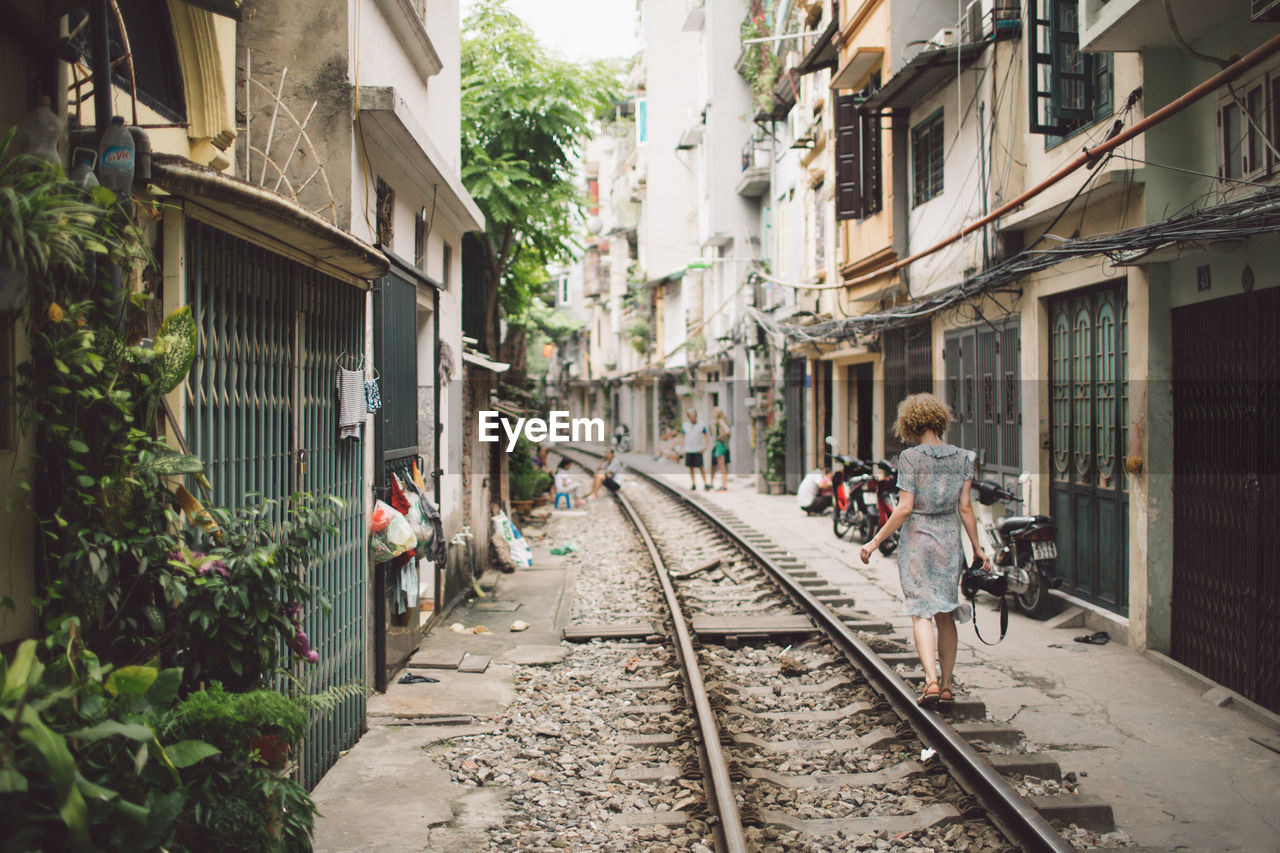 Rear view of woman walking on railroad track amidst buildings in city