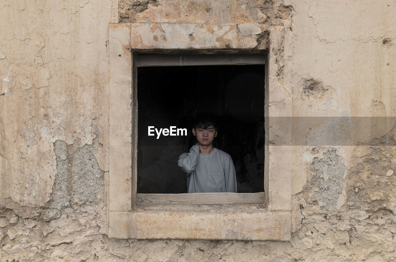Portrait of teenage asian boy behind window frame of an abandoned building